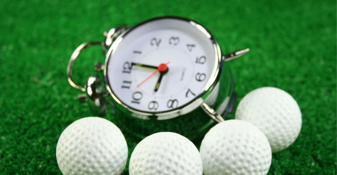 Silver golf clock and golf balls on a green fairway