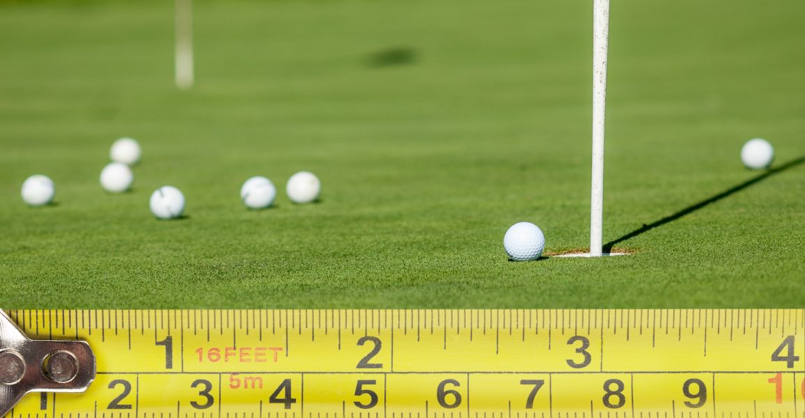 Tape measure laying across a chipping green with balls