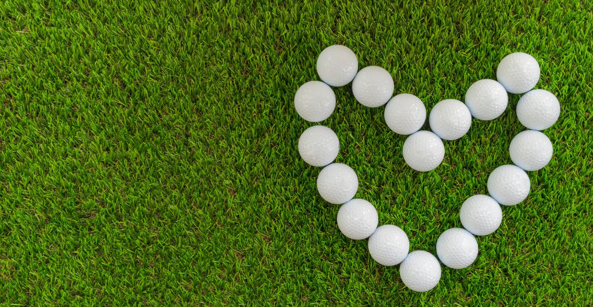 Golf balls in the shape of a heart laying on green grass