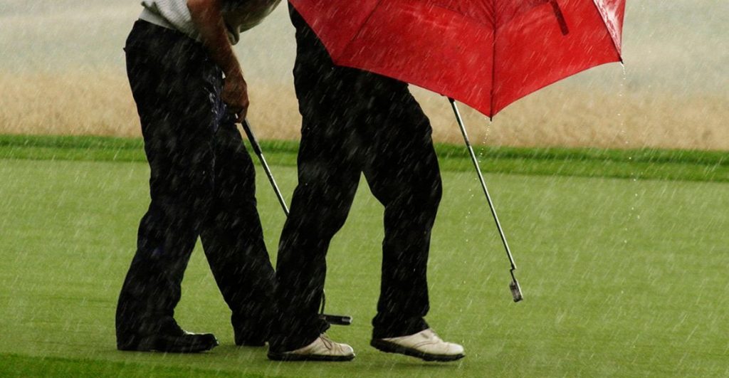Two golfers with a red umbrella playing golf in heavy rain
