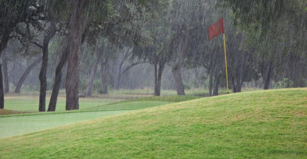 Golf green with a red flag stick in the rain