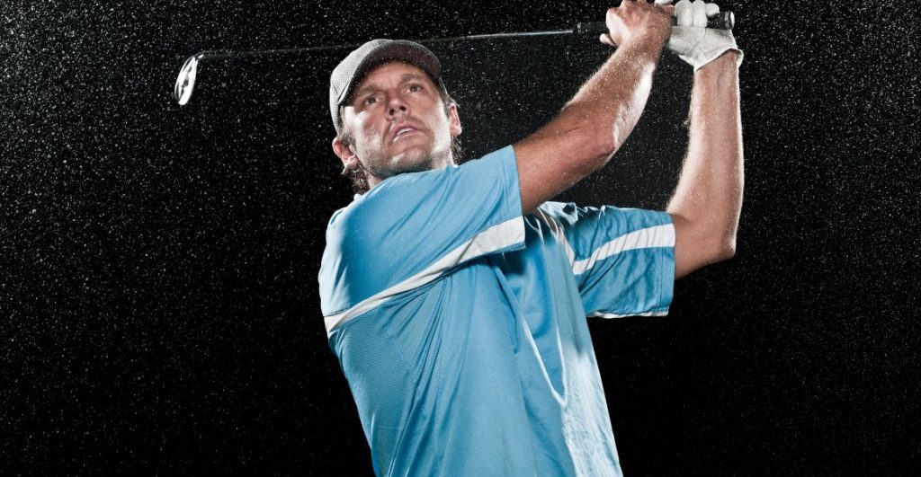 Golfer wearing a blue polo hitting a golf shot in the rain
